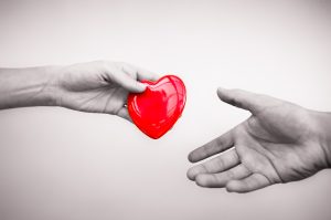 In the image, two hands are reaching for a red heart.
