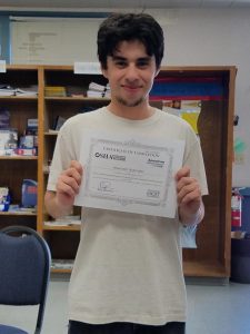 A young man proudly displaying a certificate from The LIME Foundation of Santa Rosa in a classroom.
