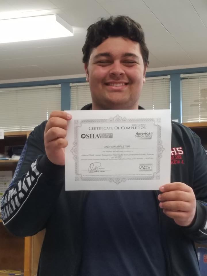 A young man proudly displaying a certificate in a library funded by the LIME Foundation.