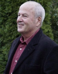A man in a black jacket smiling in front of bushes at the Sonoma County Non-Profit.