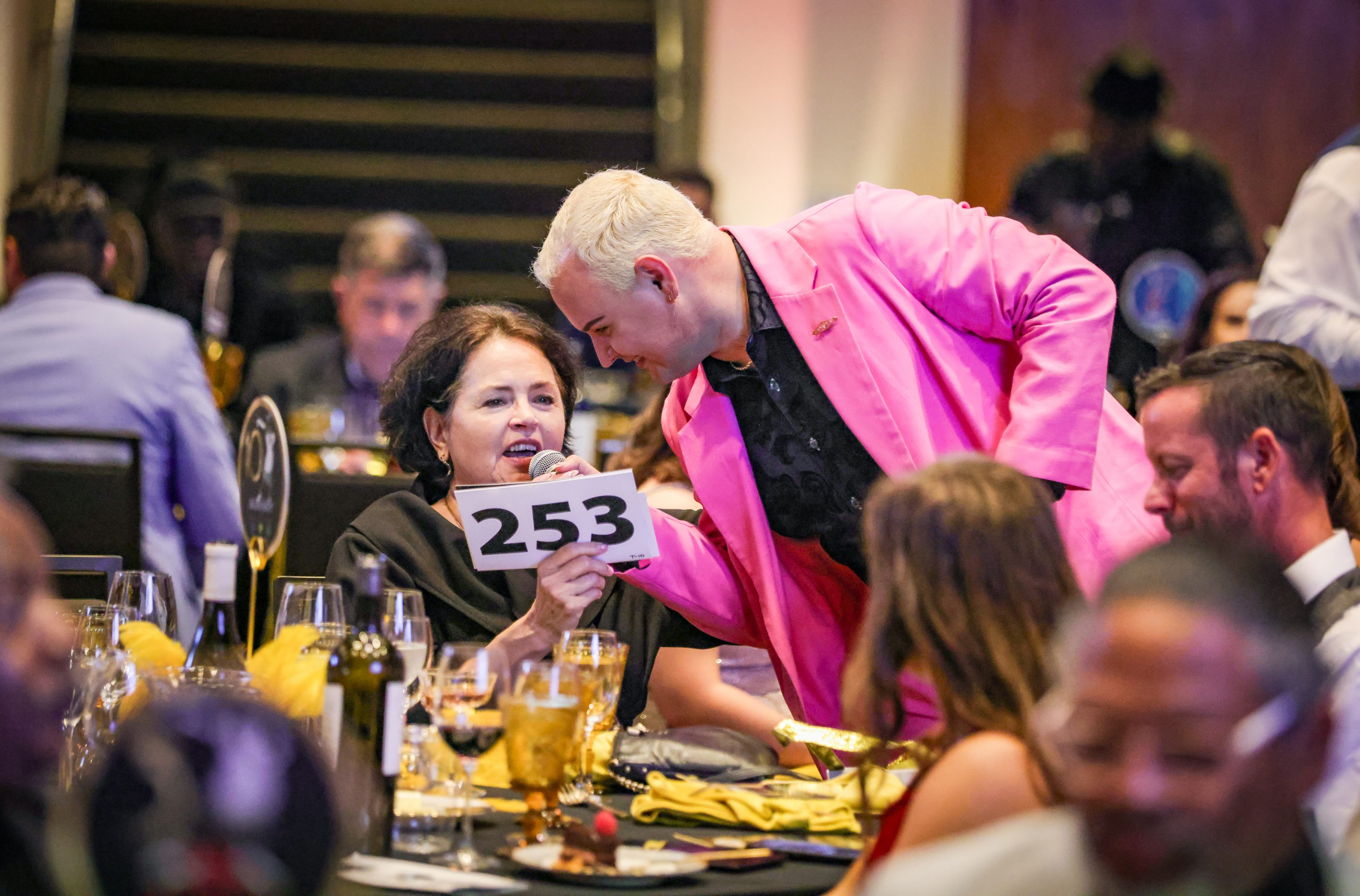 At a table, a man in a pink jacket and a woman interact.