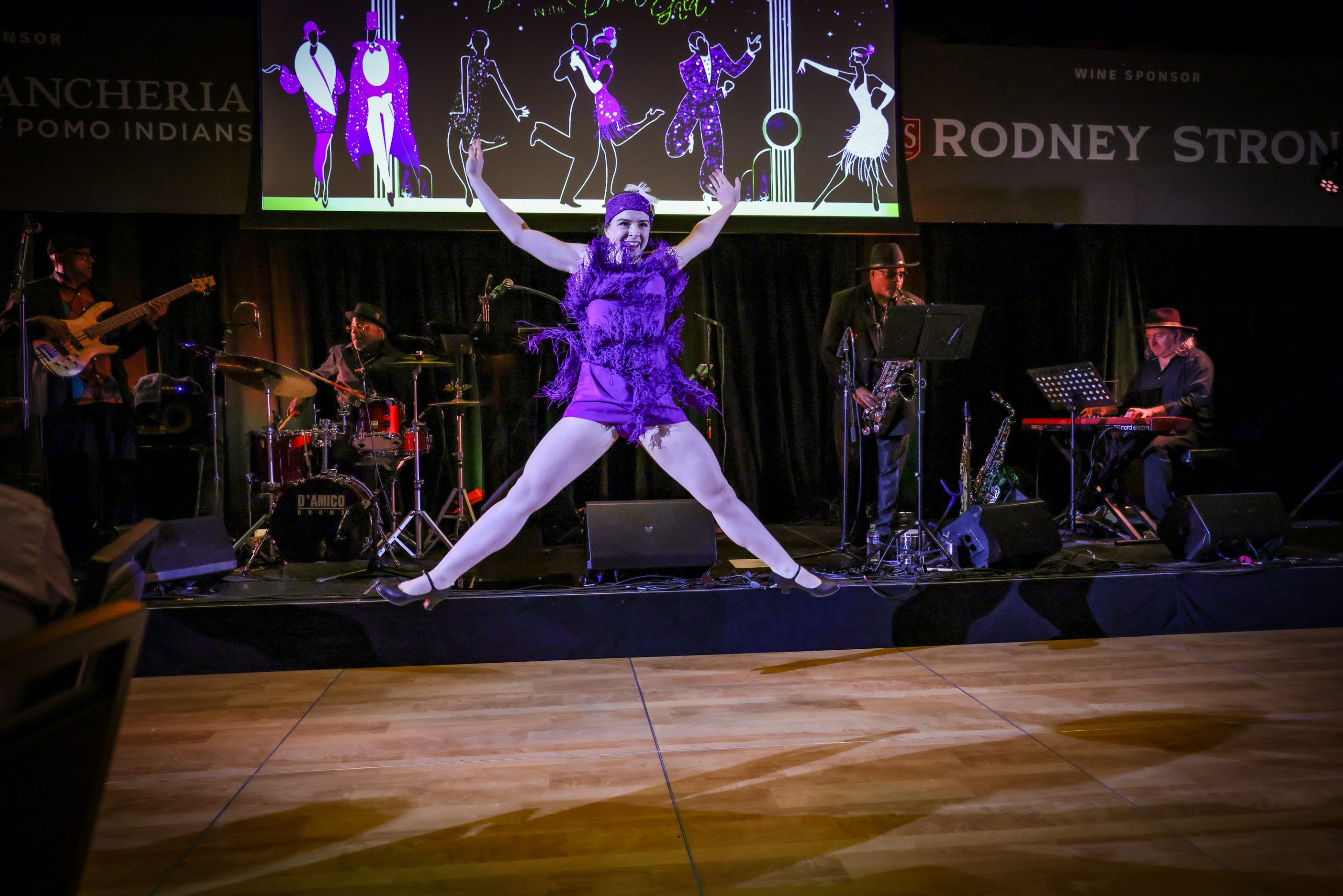 A woman in a purple dress dancing on stage at a Santa Rosa Non-Profit event.