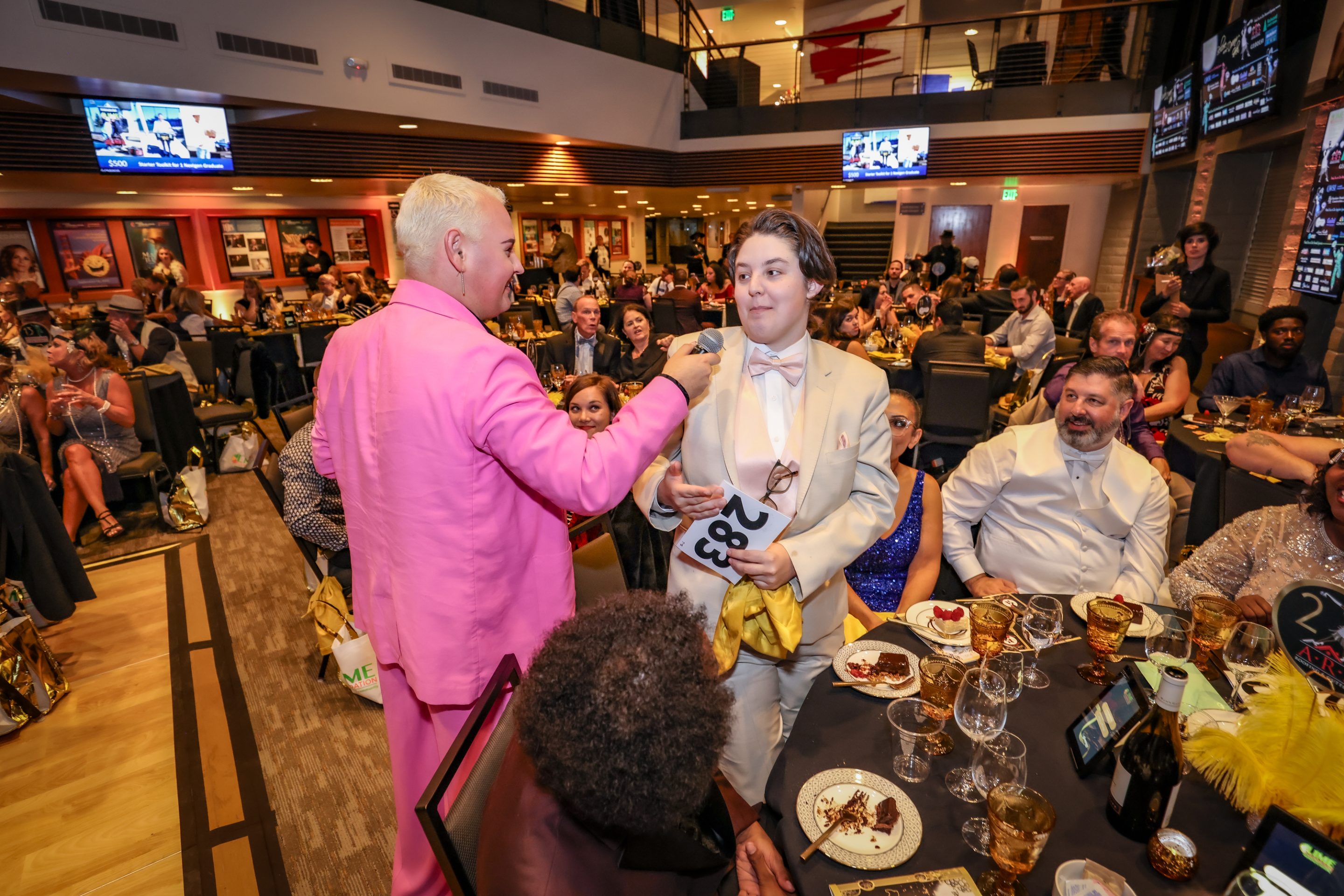 At a table, a man in a pink suit shakes hands with another man at a Sonoma County non-profit organization event.