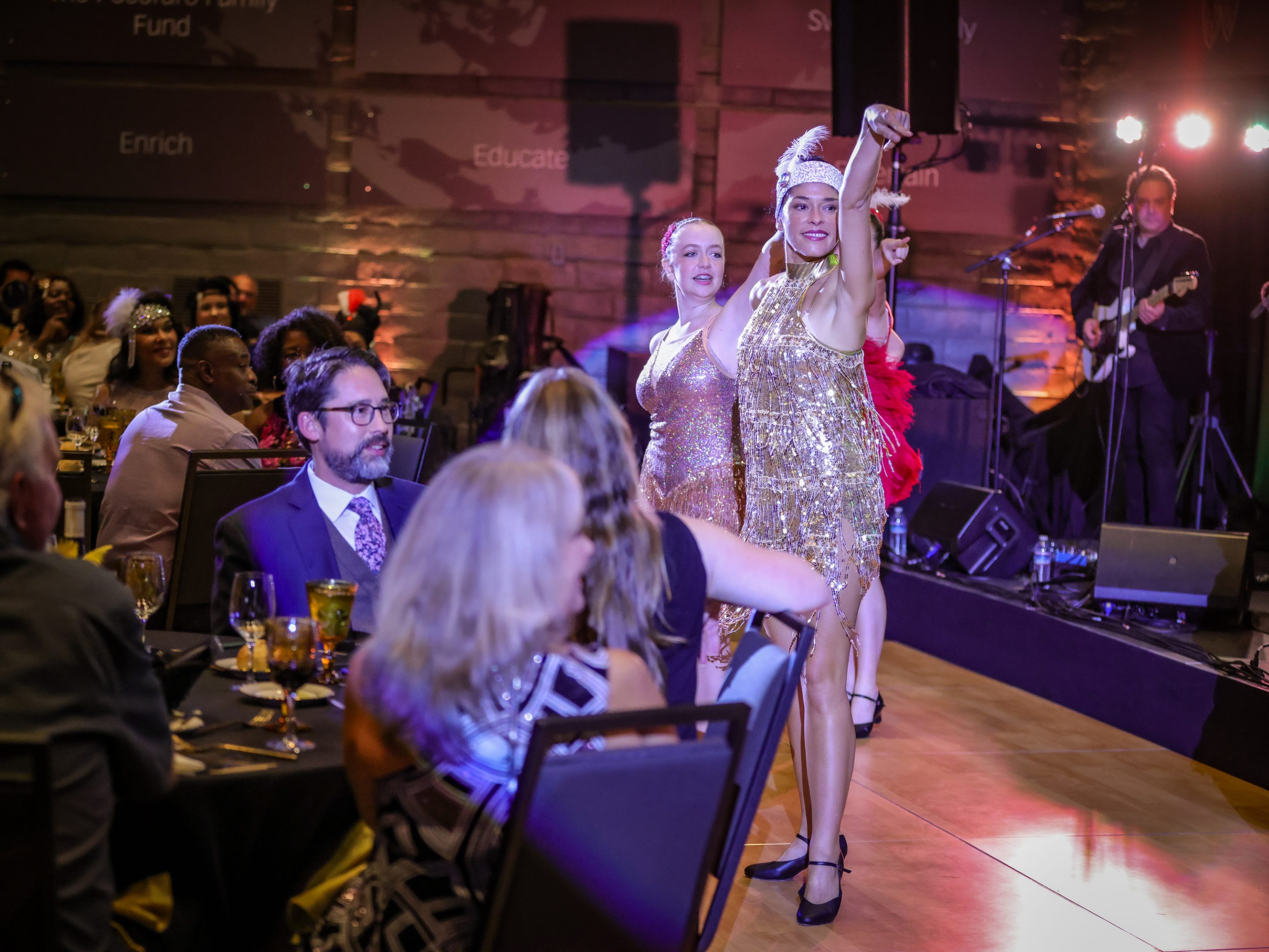 A woman in a gold dress is dancing at an event hosted by The LIME Foundation.