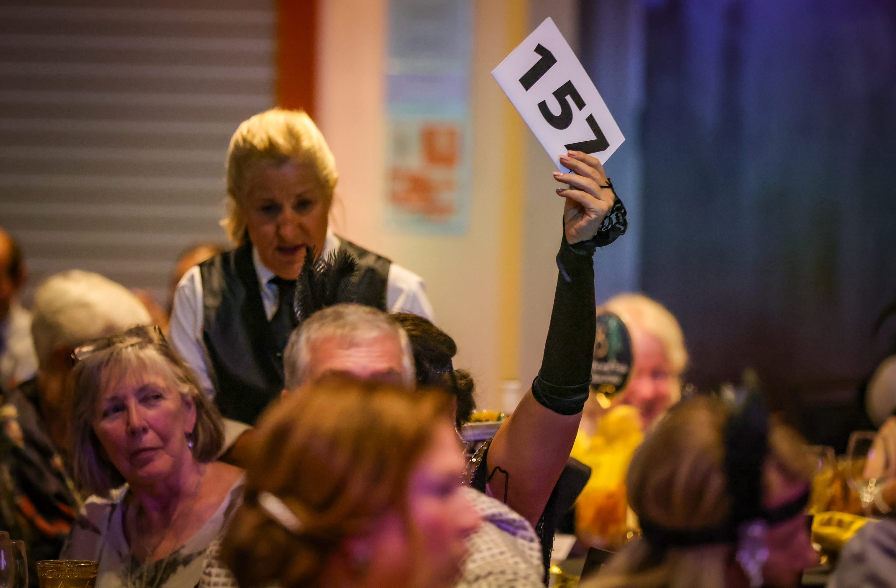 A woman holding up a number at a dinner party hosted by The LIME Foundation.
