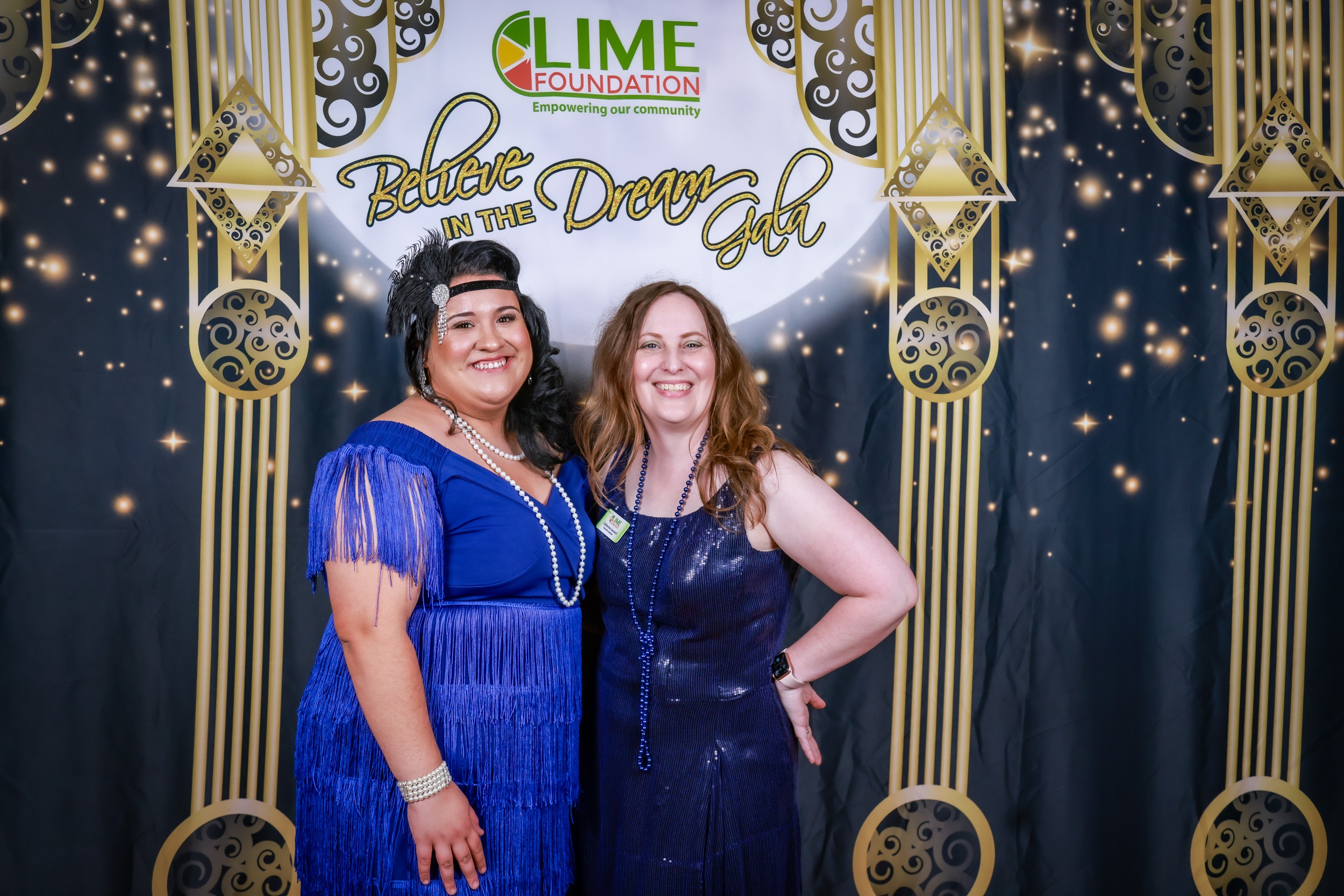 Two women posing for a photo in front of a gilded backdrop at a Sonoma County non-profit event.