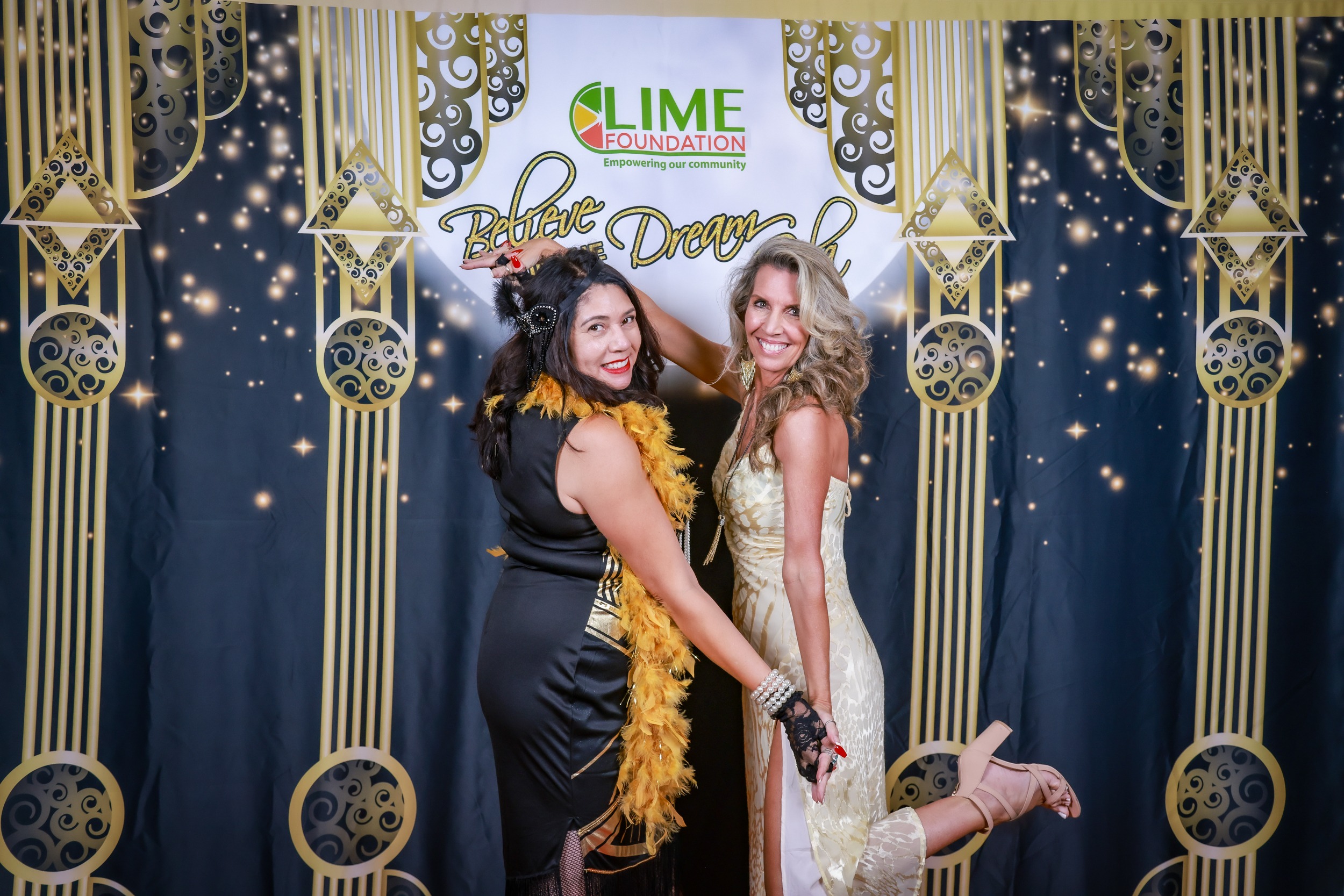 Two women posing for a photo in front of a gilded backdrop at Sonoma County Non-Profit Organization event.