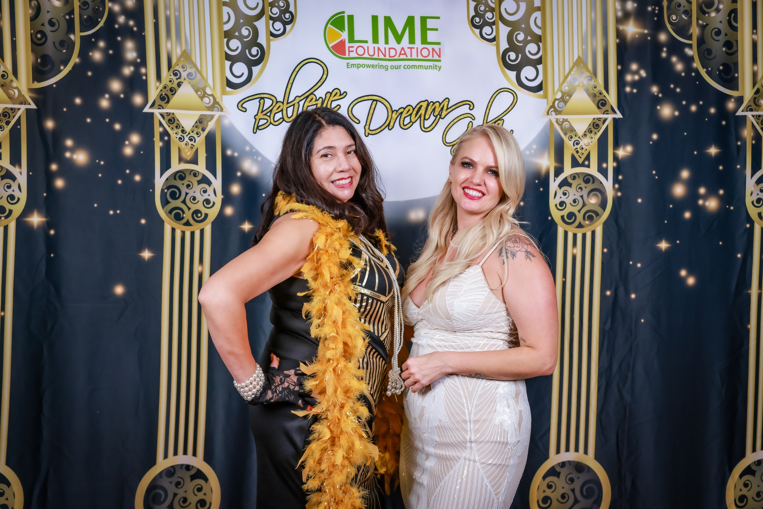 Two women posing in front of a gilded backdrop at a Sonoma County Non-Profit Organization event.