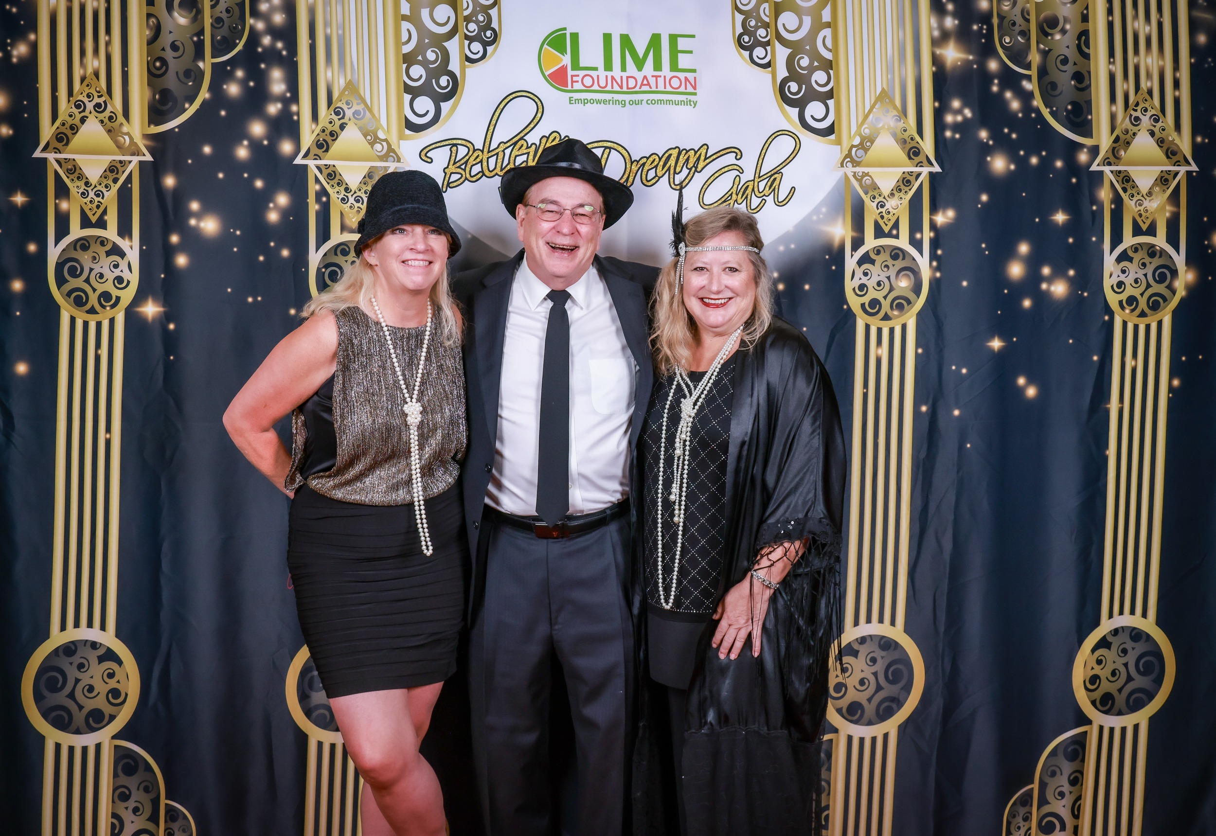 Three people posing for a photo in front of a gold backdrop at the LIME Foundation.