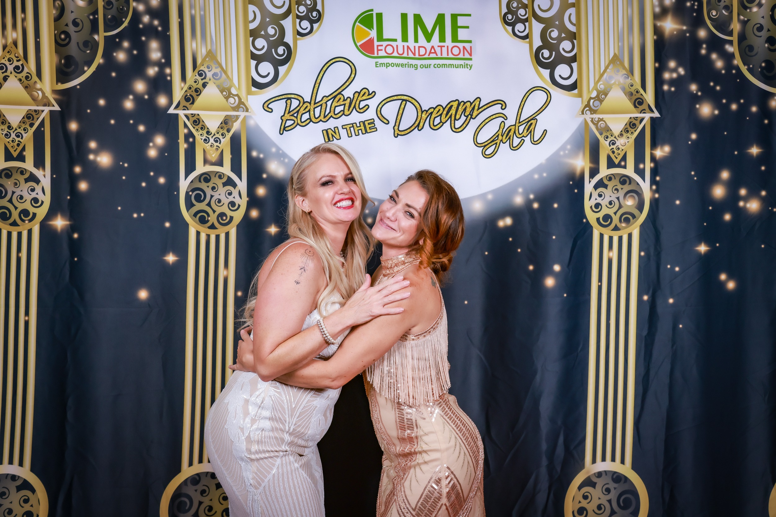 Two women posing in front of a photo booth at the LIME Foundation event.