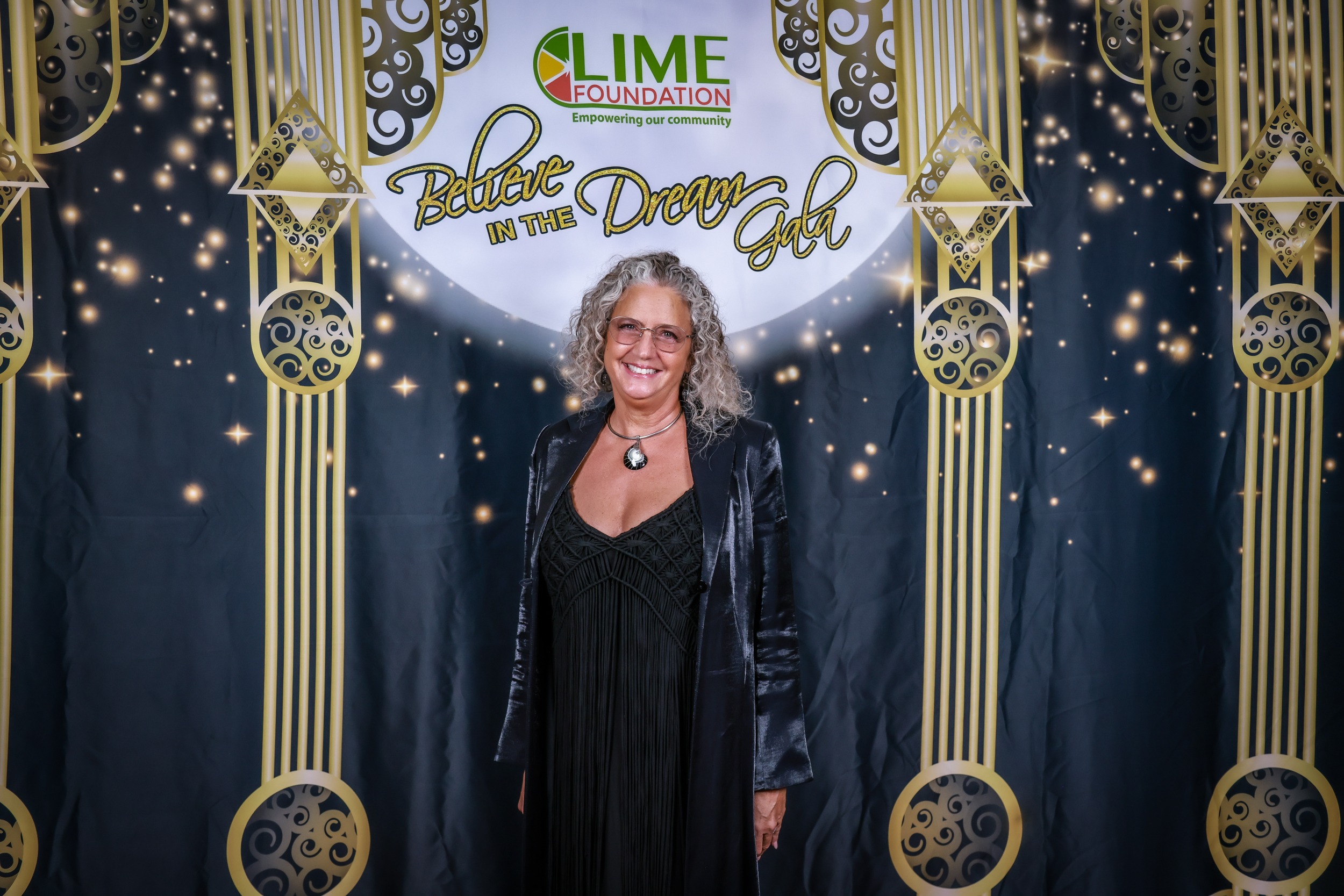A woman in a black dress standing in front of a gold backdrop at The LIME Foundation of Santa Rosa.