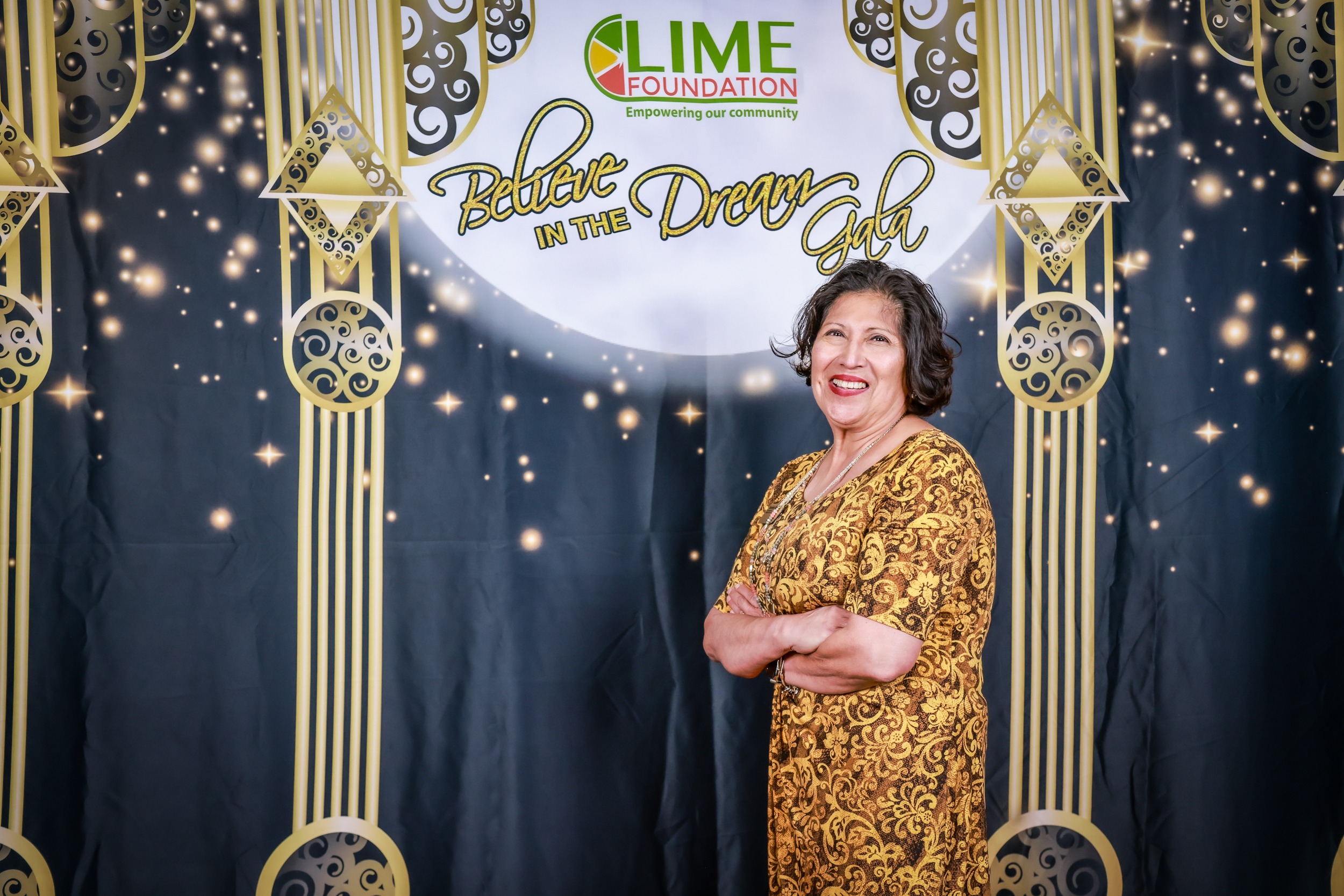 A woman in a gold dress stands in front of a backdrop at The LIME Foundation of Santa Rosa.
