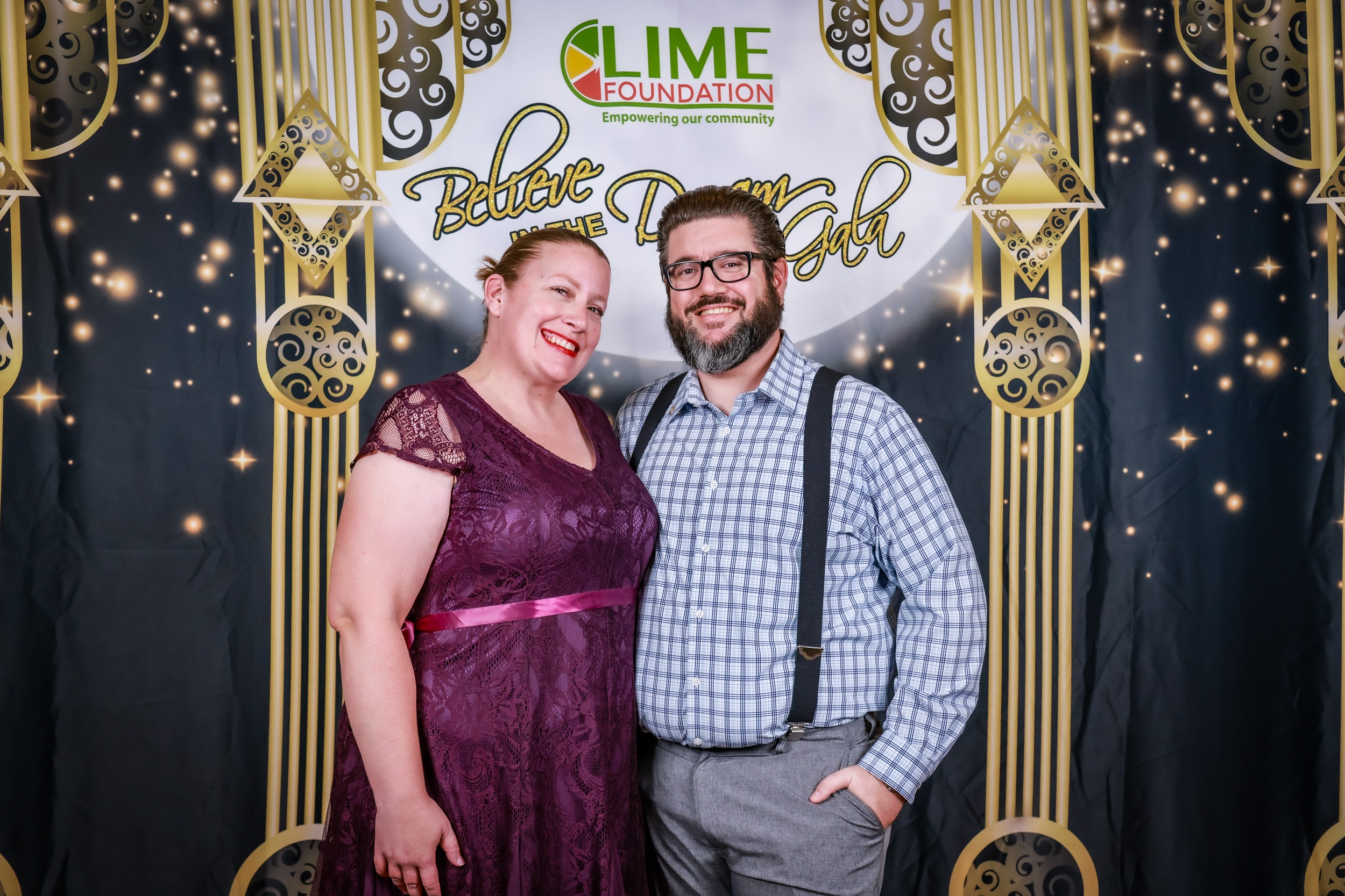 A man and woman posing in front of a photo booth at a non-profit event.