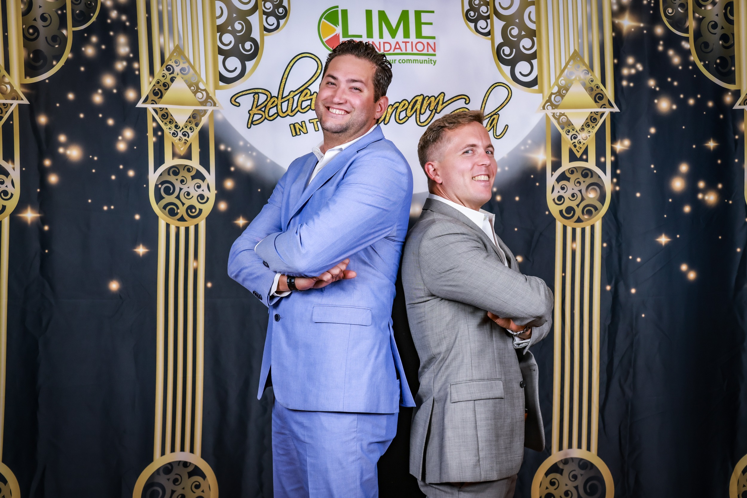 Two men in suits are posing in front of a gold backdrop at the Santa Rosa Non-Profit event.