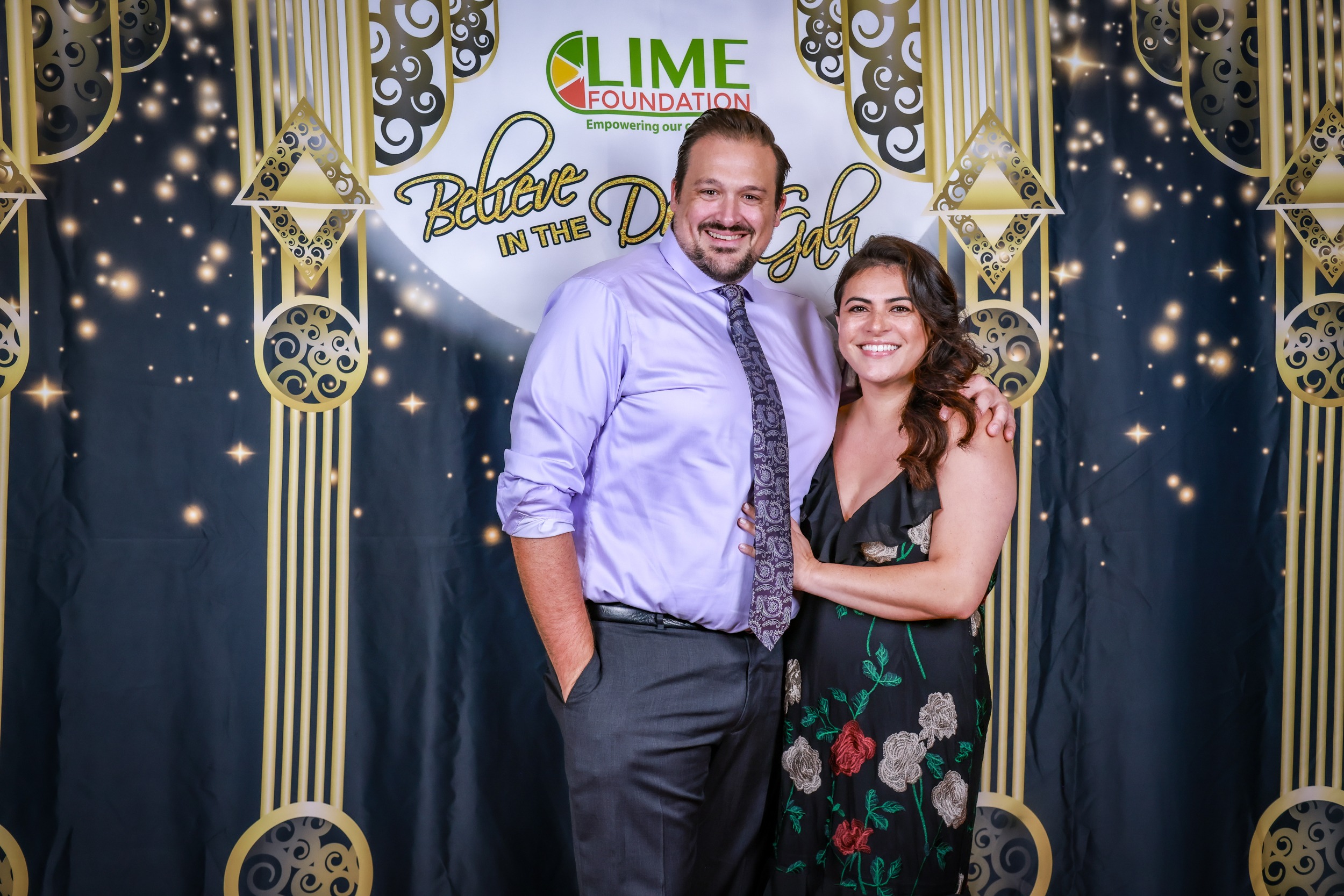 A man and woman posing for a photo in front of a backdrop provided by The LIME Foundation.