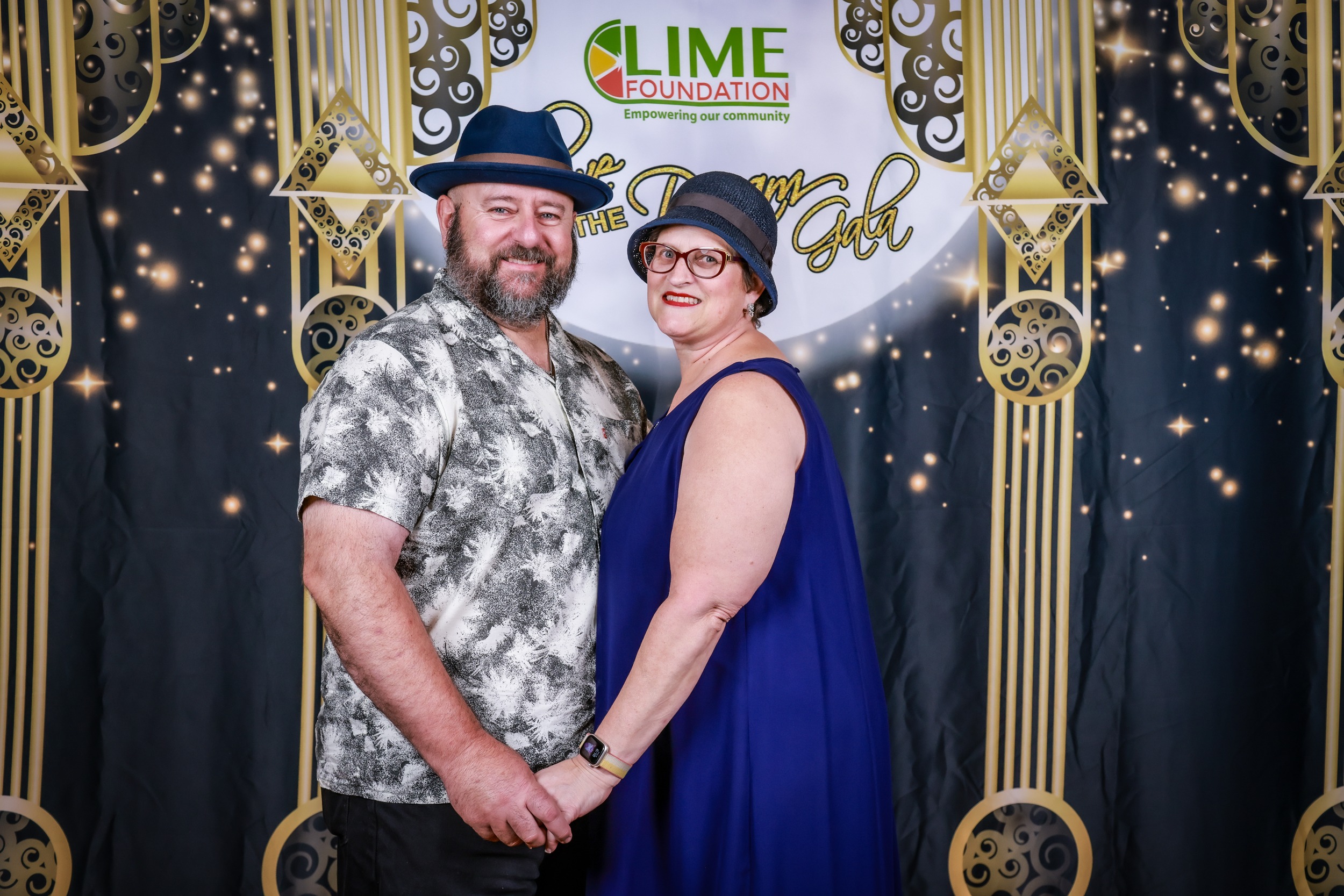 A man and woman posing for a photo in front of a gold backdrop at a non-profit organization event in Sonoma County.