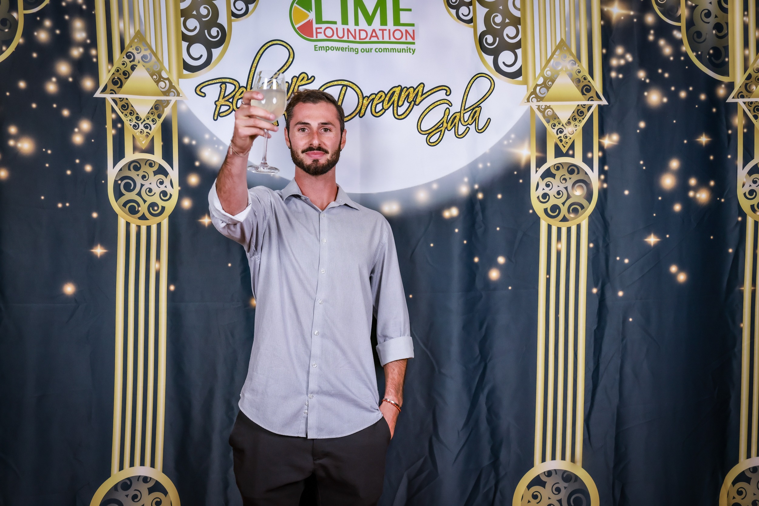 A man holding a glass of champagne in front of a backdrop at The LIME Foundation event in Santa Rosa.