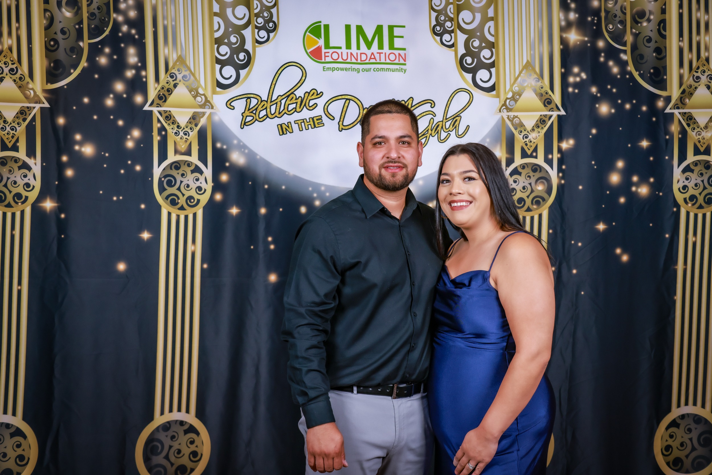 A man and woman posing for a photo in front of a gold backdrop at a Sonoma County Non-Profit Organization event.